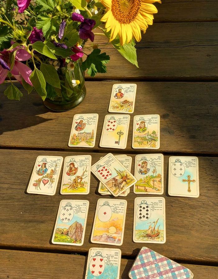 Persoonlijk consult met Lenormand kaarten Kaartspel op een houten tafel met een vaas zonnebloemen en kleurrijke bloemen.